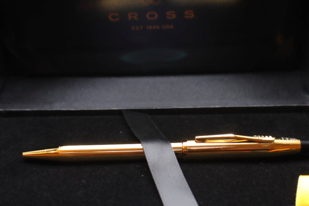 Gold pen on a black surface with 'Cross' branding in the background