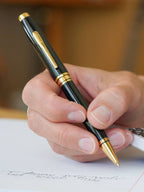 Hand holding a black and gold pen writing on paper with a blurred background