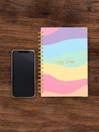 Colorful spiral-bound notebook with 'Happy Days' text next to a smartphone on a wooden surface