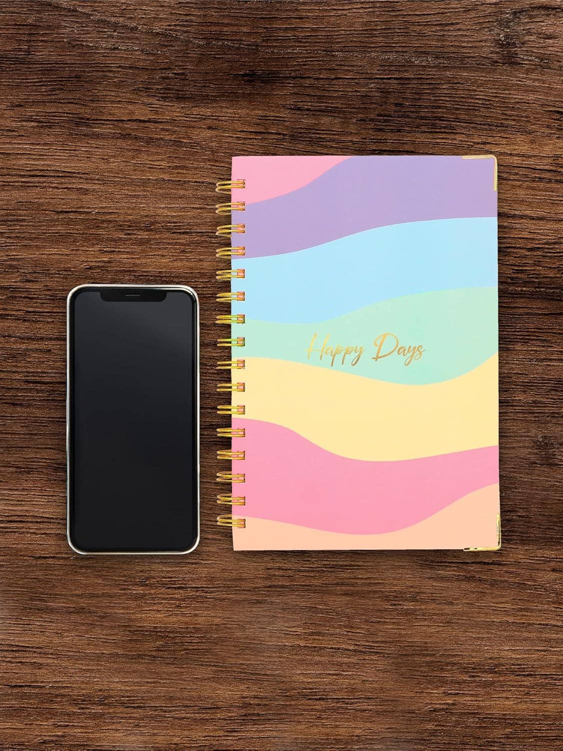 Colorful spiral-bound notebook with 'Happy Days' text next to a smartphone on a wooden surface