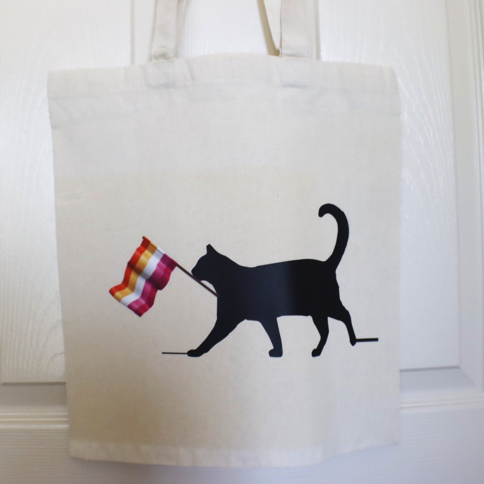 Tote bag with a black cat holding a colorful flag design on a white background