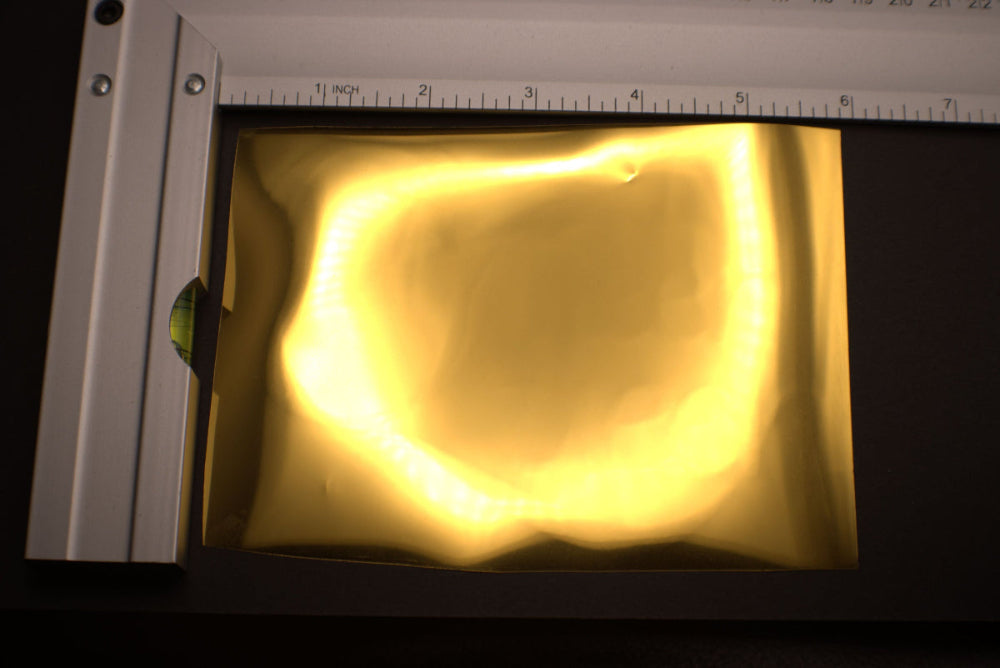 Yellow object under a light source with a ruler for scale on a dark background