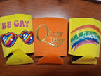 Three colorful can coolers with text and designs on a wooden surface