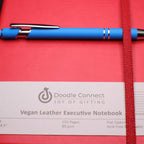 Red vegan leather executive notebook with a blue pen on a red background, featuring the Doodle Connect brand.
