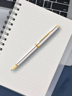 Silver and gold pen on a notebook with a laptop in the background